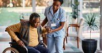 Young nurse assists a man to get up from wheelchair at a clinic. 