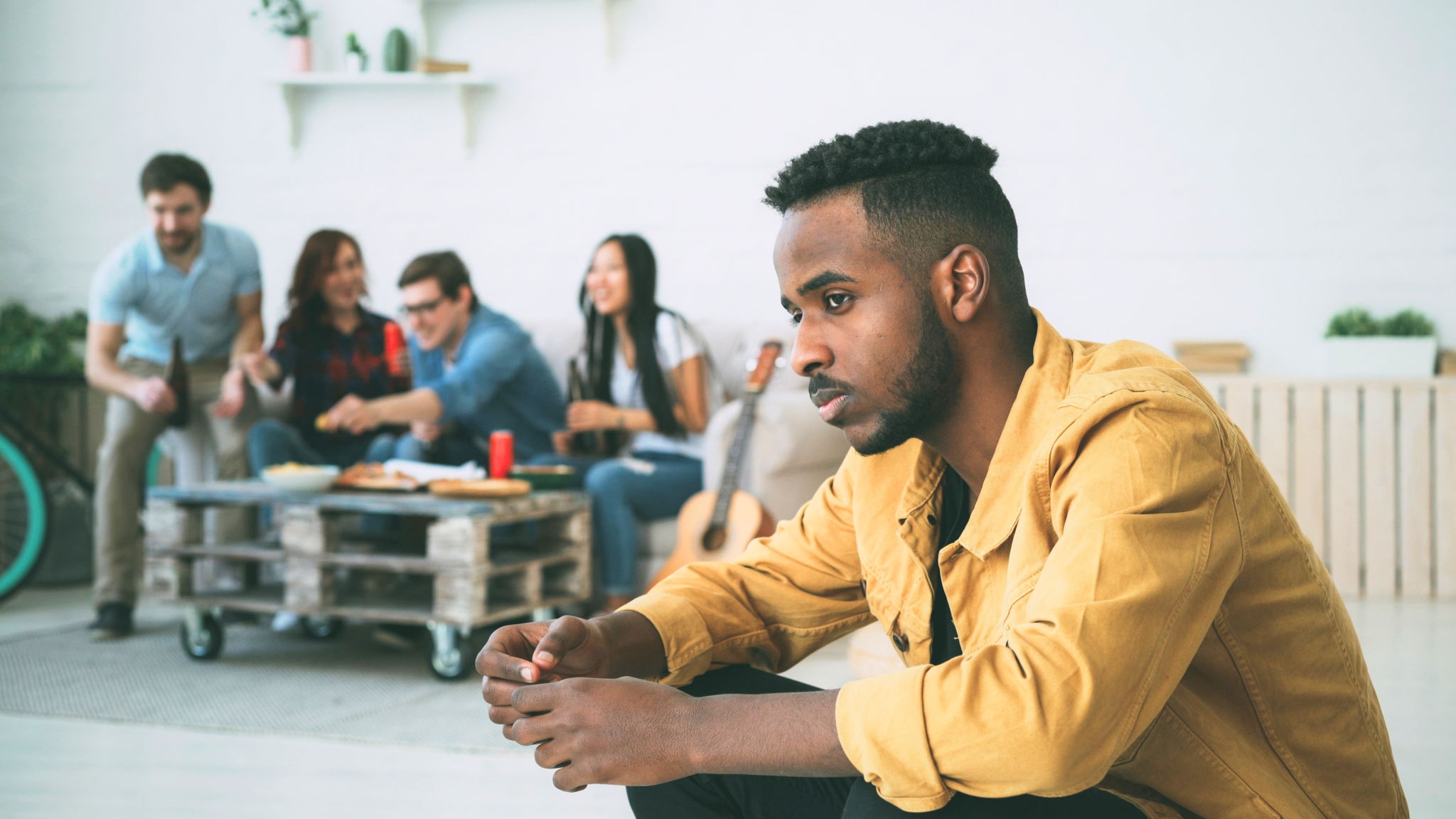Young man feels upset and isolated while his friends drink and party