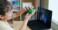 A child playing with a green stress toy in front of a laptop.