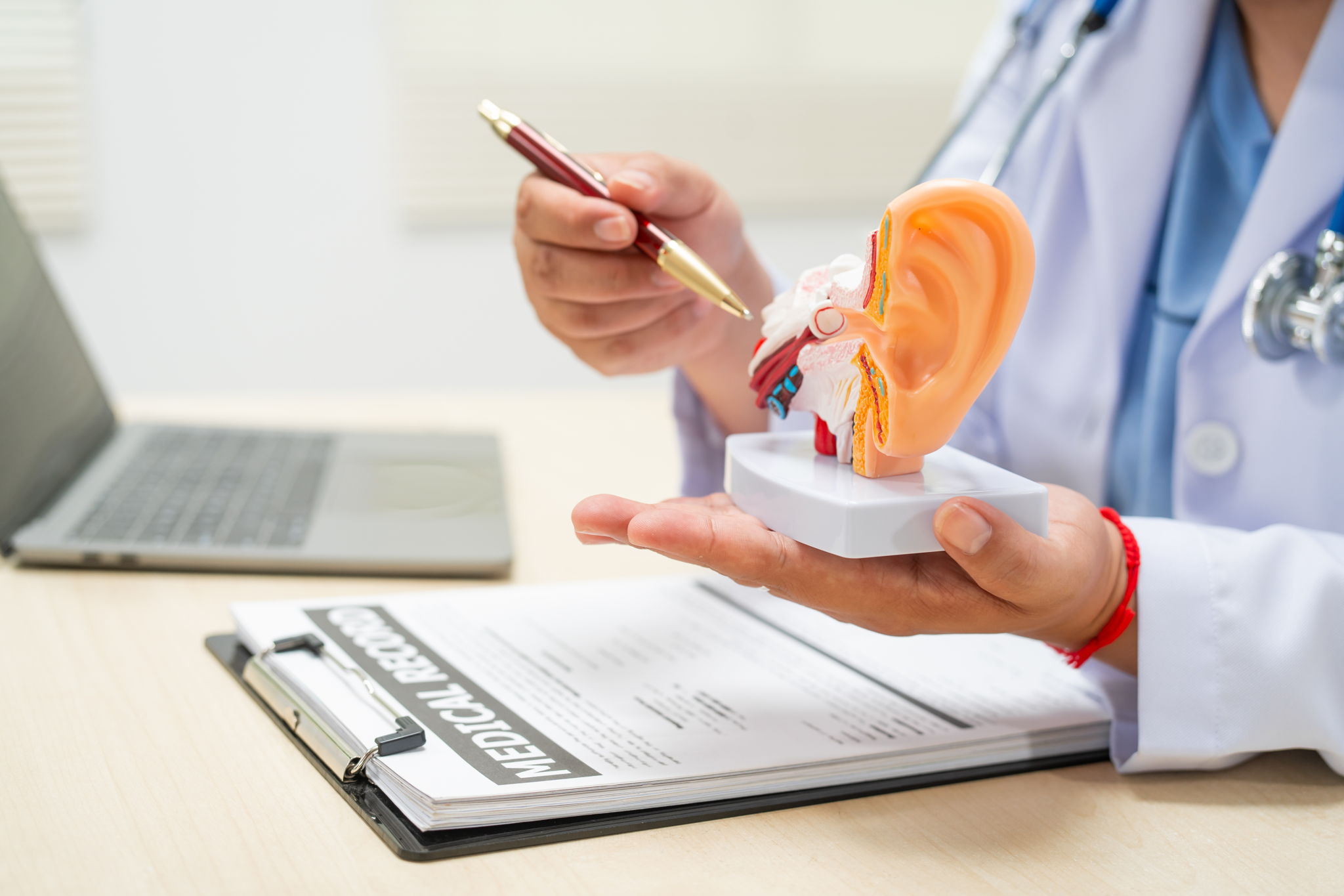 A doctor sits at a table  holding a model of an ear, discussing balance problems like dizziness and vertigo.