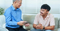 An older male therapist sitting beside a younger client. Both are smiling.