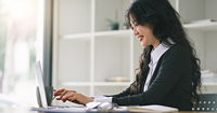 A smiling woman with long dark hair working at a laptop, pictured in profile.