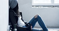 Adolescent girl leaning slouched against a wall, holding a beer
