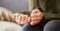 A pair of hands clenched together resting on the person's knees. The person is wearing a green sweater and worrying at the cuff.