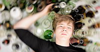 A young man lying on a bed of empty bottles