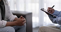 Close up of therapist and client, therapist holding a clipboard, only hands and legs visible.