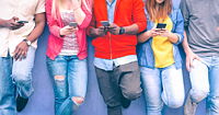 A row of adolescents leaning against a wall using their smartphones