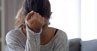 A dark skinned woman pressing her forehead to her fist.