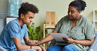 A worried teenage boy receives support from an adult in a private office setting.