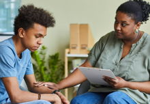 A worried teenage boy receives support from an adult in a private office setting.