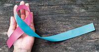 A hand holding a blue and pink awareness ribbon.