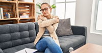 A woman sitting on a grey couch hugging herself.