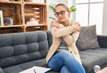 A woman sitting on a grey couch hugging herself.