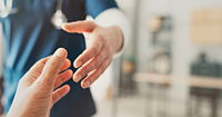 A profressional wearing dark blue scrubs reaching out to a hand. The background is blurred, leaving only the hands in focus.