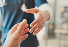 A profressional wearing dark blue scrubs reaching out to a hand. The background is blurred, leaving only the hands in focus.