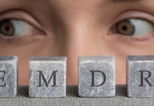 A close up of two hazel eyes looking to the side with grey blocks in front of them with letters forming "EMDR"