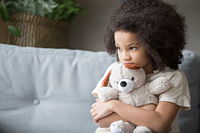 A young child holding a teddy bear, looking apprehensive.