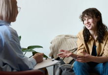 A therapist viewed from behind talking to a smiling woman in a brown shirt.