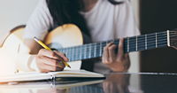 A songwriter thinking while writing notes and lyrics in a book