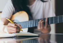 A songwriter thinking while writing notes and lyrics in a book
